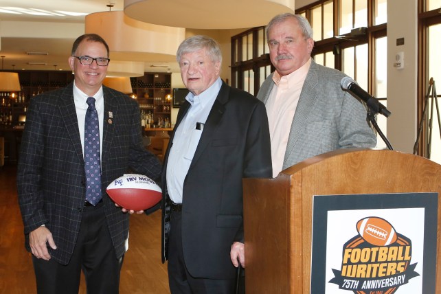 Irv Moss of the Denver Post, center, receives a commemorative football in recognition of his Lifetime Achievement Award from 2015 FWAA President Lee Barfknecht, left, and Tim Simmons of BFI Events, right. Photo by Melissa Macatee for the FWAA.